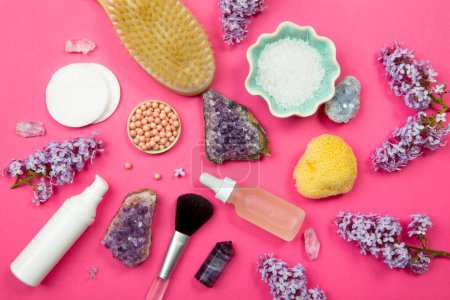 Photo for Above top down view of various white cosmetic and beauty products containers with lilac (Syringa) blossoms and semi precious amethyst crystal clusters on pink studio background. - Royalty Free Image