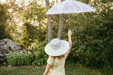 Téléchargez les photos : Fille enfant tient parasol de soleil en dentelle blanche sur belle soirée ensoleillée dans la nature. Concept d'aspirations rêveuses. - en image libre de droit