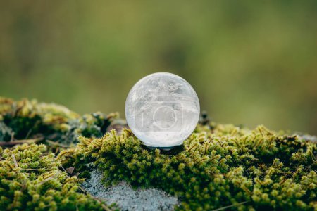 Photo for Gemstone sphere or crystal balls known as crystallum orbis and orbuculum which is the beacon of peace and harmony in environment. Natural clear quartz ball on stand on stone with moss with copy space. - Royalty Free Image