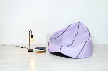 Photo for Minimalist home concept. Bean bag, lamp and stack of books, white walls and floor. Less is more. - Royalty Free Image