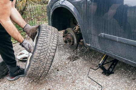 Téléchargez les photos : Propriétaire de voiture changer pneu à plat à l'extérieur sur la rue. Retirez et maintenez pneu et outil de cric a soulevé la voiture. - en image libre de droit
