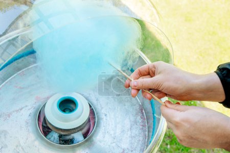 Close up view of person hands spinning blue color cotton candy with machine. Spin around wood stick. 