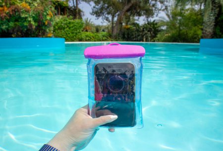Konzept der Influencerin Frau machen Videos und Fotos in und unter Wasser mit Smartphone, das in einer wasserdichten Tasche ist. Hand hält Smartphone in Tasche in schönen blauen Pool, tropische Lage.