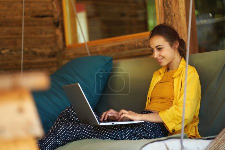 Téléchargez les photos : Jeune femme d'affaires travaillant à distance sur ordinateur portable sur des projets d'entreprise tout en étant assis sur swing dans le café - en image libre de droit