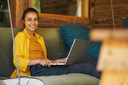 Photo for Portrait young smiling woman freelance worker or student working remotely from summer cafe on laptop computer - Royalty Free Image