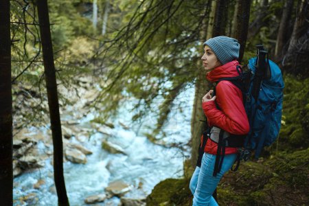 Téléchargez les photos : Voyage actif aventure randonnée avec sac à dos, randonnée touristique femme dans la forêt au bord de la rivière - en image libre de droit