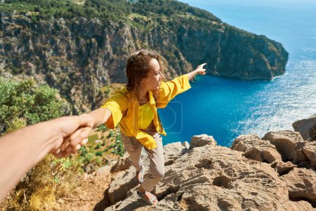 Photo for Happy tourist woman holding her boyfriend hand, showing him towards the breathtaking scenery of Butterfly Valley Beach. Couple exploring scenic landscape with crystal clear turquoise water - Royalty Free Image