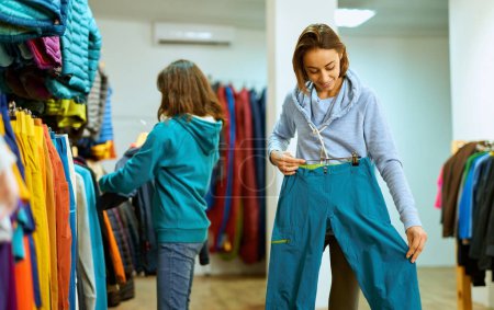 Jeune femme essaie le pantalon, en sélectionnant l'ajustement parfait dans le magasin de vêtements. Explore son style.