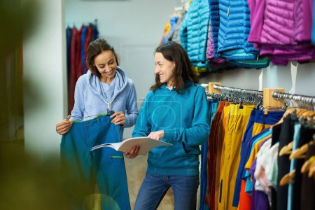 Jeune femme magasinant dans un magasin de vêtements, tandis qu'un consultant utile la guide à travers les dernières tendances et styles
