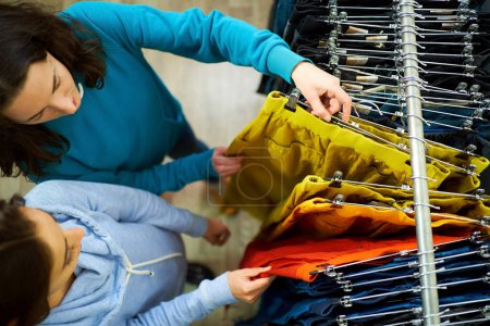 Assistante shopping personnelle Top View guidant une jeune femme à travers la sélection de vêtements à la mode dans un magasin de boutique.