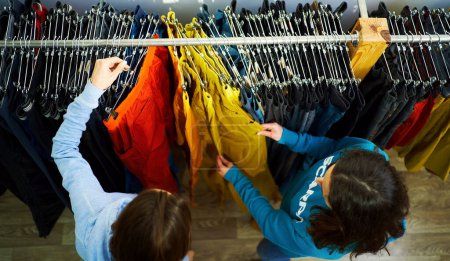 Assistante shopping personnelle Top View guidant une jeune femme à travers la sélection de vêtements à la mode dans un magasin de boutique.