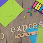 Express yourself letters on wooden board with coloured paper. Coloured tags and envelopes. Coloured push pins