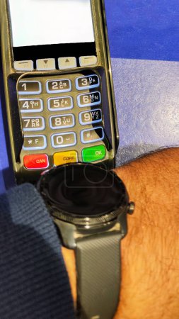 Foto de Persona que utiliza un reloj inteligente para pagar la factura mediante un dispositivo bancario portátil o terminal de punto de venta con enfoque selectivo - Imagen libre de derechos