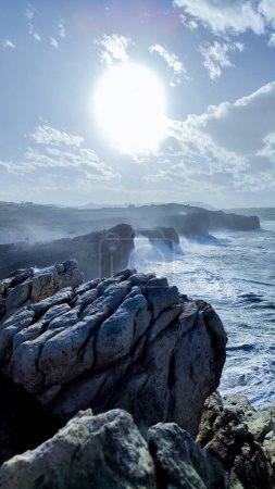 Téléchargez les photos : Photographie verticale d'une falaise avec la mer et de fortes vagues accolant une journée ensoleillée avec espace de copie et mise au point sélective - en image libre de droit