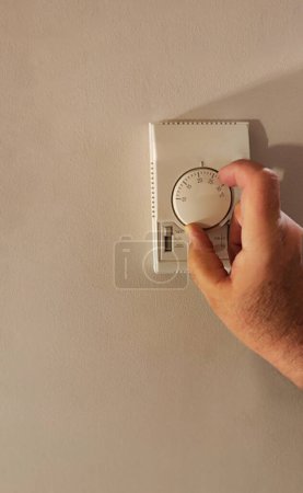 Eine Person stellt das Thermostat an der Wand ein und sorgt so für optimalen Komfort zu Hause.