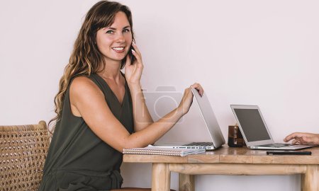 Photo for Portrait of young skilled hipster girl making positive friendly cell conversation during remote working with husband, married pair collaborating near promotional wall using digital technologies - Royalty Free Image