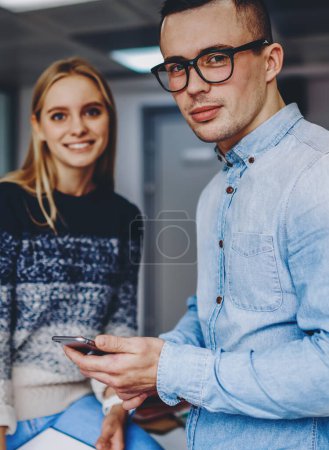 Photo for Portrait of professional colleagues dressed in casual wear looking at camera while working together in office interior.Two hipster students standing in coworking space.Young man with cellular in hand - Royalty Free Image