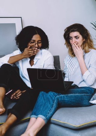 Photo for Excited african american young woman and caucasian hipster girl shocked with last fashion news on website.Wondered diverse friends watching strange video on laptop computer using home internet - Royalty Free Image