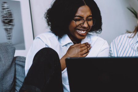 Photo for Cheerful african american young woman laughing together with caucasian friend while watching funny comedy online on laptop device spending free time at home.positive diverse hipster bloggers have fun - Royalty Free Image