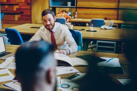Photo for Cheerful guy in formal wear with red tie talking to partners having fun resting from work sitting at table at workplace - Royalty Free Image