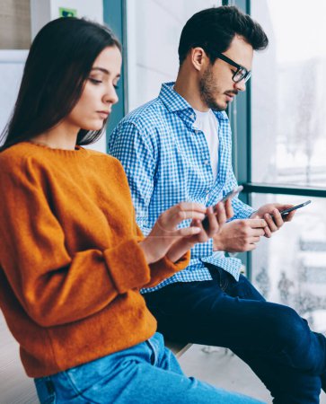 Photo for Millennial hipster girl and guy sitting together ignore real conversation prefere to chatting in social networks via modern smartphones and 4G internet connection, addiction to modern devices - Royalty Free Image