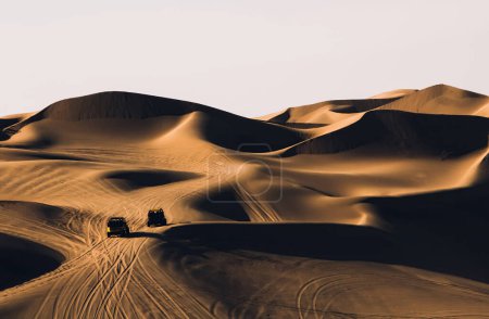 Foto de Majestuoso desierto en Marruecos con grandes dunas de arena con sombras y ondas contra el cielo gris y coches que conducen sobre arena. - Imagen libre de derechos