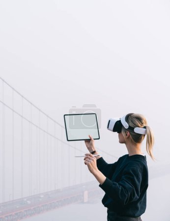 Foto de La joven caucásica trabaja en una almohadilla táctil moderna con auriculares de realidad virtual mientras planifica la construcción de ingeniería 3D en un espacio de copia abierta. Arquitectura aumentada con alta tecnología innovadora VR - Imagen libre de derechos