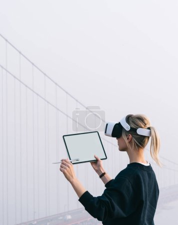 Foto de Mujeres caucásicas milenarias mirando en la pantalla de la alfombra táctil moderna usando auriculares virtuales de realidad y manteniendo el lápiz digital a mano. Arquitectura e ingeniería con tecnología innovadora VR - Imagen libre de derechos