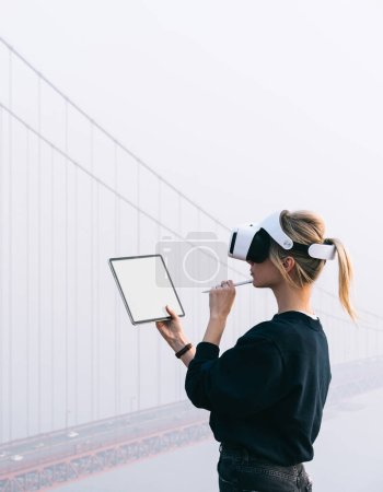 Foto de Thoughtful caucasian female work on modern touch pad wearing virtual reality glasses while planning 3D engineering construction in headset. Arquitectura aumentada con alta tecnología innovadora VR - Imagen libre de derechos