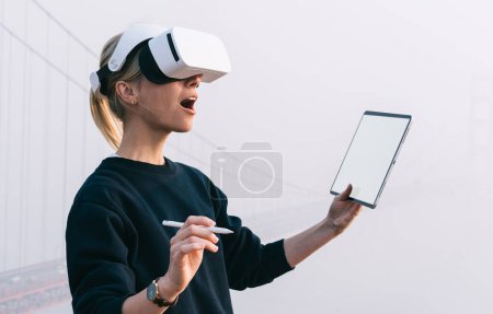 Foto de Una sensación femenina asombrosa se pregunta emoción probando la experiencia de la realidad virtual con la tecnología innovadora que lleva auriculares VR. Sorprendida hipster chica explorando el ambiente de simulación con una dimensión aumentada. - Imagen libre de derechos