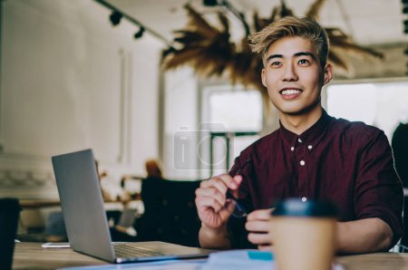 Photo for Cheerful smiling asian hipster student sitting at table with female colleague and feeling good from collaboration indoors, successful friends learning in coworking space using laptop computer - Royalty Free Image