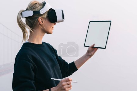 Foto de Mujeres caucásicas milenarias mirando en la pantalla de la alfombra táctil moderna usando auriculares virtuales de realidad y manteniendo el lápiz digital a mano. Arquitectura y diseño de tecnología innovadora con conjunto VR - Imagen libre de derechos