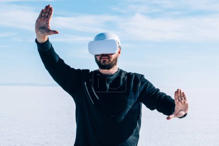 Foto de Hombre en realidad virtual de audífonos gestando con las manos para controlar la dimensión simulada mientras se encuentra al aire libre en un espacio futurista vacío. Tecnología avanzada e innovación. - Imagen libre de derechos