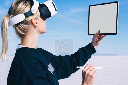 Foto de Mujeres caucásicas milenarias mirando en la pantalla de la alfombra táctil moderna usando auriculares virtuales de realidad y manteniendo el lápiz digital a mano. Arquitectura y diseño de tecnología innovadora con conjunto VR - Imagen libre de derechos