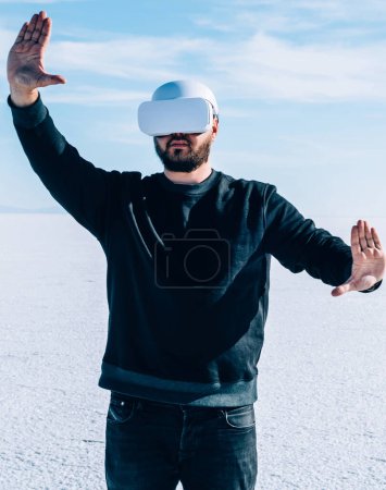 Foto de Hombre en realidad virtual de audífonos gestando con las manos para controlar la dimensión simulada mientras se encuentra al aire libre en un espacio futurista vacío. Tecnología avanzada e innovación. - Imagen libre de derechos