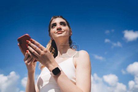 Photo for Young woman with smartphone and smartwatch under clear blue sky, connectivity and modern lifestyle concept - Royalty Free Image