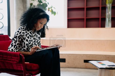 Téléchargez les photos : Femme d'affaires noire en imprimé animal haut axé sur la tablette numérique dans un salon de bureau chic, dépeignant un mélange de style et de savvy numérique dans un cadre d'entreprise. - en image libre de droit