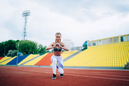 Junge schlanke Frau im Sportkleidungstraining mit Schleife und Ausfallschritten beim Training im großen Stadion vor laufender Kamera