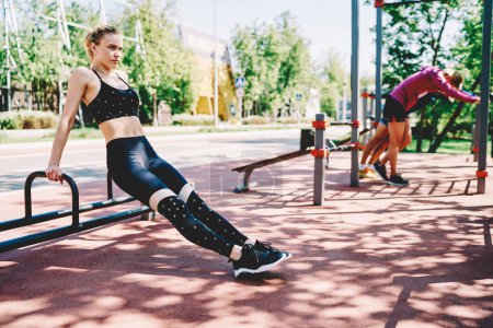 Femme blonde active concentrée et confiante vêtue de vêtements de sport moulants se préparant à l'entraînement dans le domaine sportif du parc d'été pendant la journée