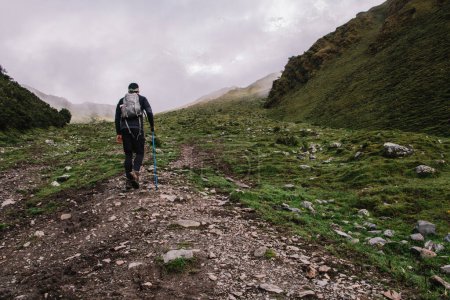 Rückansicht eines Touristen mit Rucksack, der mit Trekkingstöcken den Berg hinaufklettert und die natürliche Umgebung erkundet, ein Mann, der Fernweh nach dem höchsten Gipfel Südamerikas hat