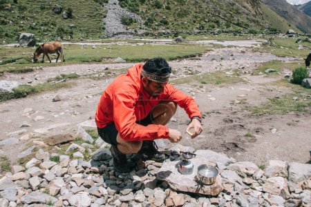Latino American male tourist in active wear getting fire with matches for cooking on metallic burner during trekking tour for exploring wild natural environment in National Park, concept of adventures