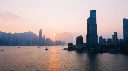 Luftaufnahme von Hongkong Abend mit der Metropolbucht Victoria Harbor bei Sonnenuntergang. Beleuchtetes modernes Stadtbild, städtische Skyline-Gebäude. Energieinfrastruktur. Beliebte asiatische Stadt