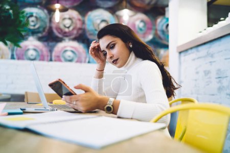 Caucasian woman sharing media files via smartphone and laptop technology connecting to bluetooth, skilled female freelancer checking received email on cellphone while doing tutorial e learning
