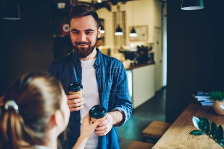 Positiv aussehender Mann in Freizeitkleidung entspannt sich von der Arbeit, während die Frau mit einer Tasse Kaffee Zeit im Café verbringt