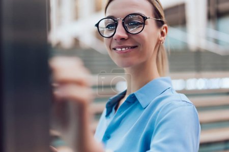 Femme souriante debout à l'affichage innovant avec la technologie numérique de pointe. Jeune femme touchant avec doigt écran futuriste de kiosque interactif pour trouver des informations tout en se tenant debout à l'extérieur