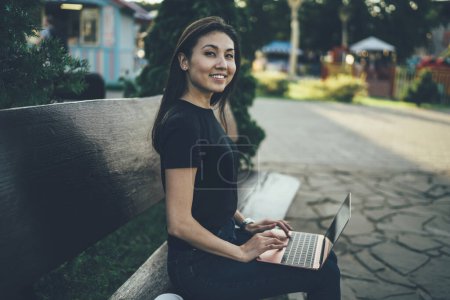 Photo for Portrait of cheerful asian female freelancer sitting on bench i city park using laptop computer for remote job satisfied with online earning, happy young woman student learning outdoors via 4G - Royalty Free Image