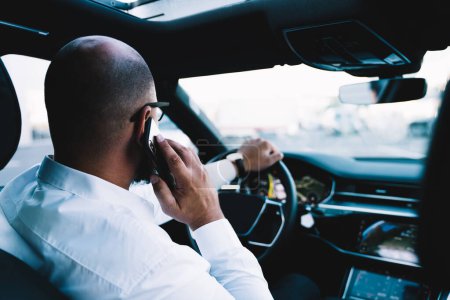 Photo for Executive businessman using international roaming connection for making cellphone call during wheel driving in luxury rent car, male communicating with partners while steering vehicle automobile - Royalty Free Image