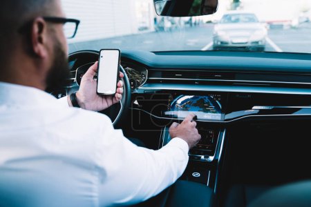 Photo for Concept of safety during wheeling in automotive vehicle, executive man checking location information while driving contemporary automobile machine using 4g wireless internet on smartphone technology - Royalty Free Image