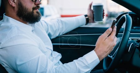 Photo for Businessman reading received smartphone notification while using self-driving in contemporary car with autopilot, cropped image of male tracking gps location via cellphone application connected to 4g - Royalty Free Image