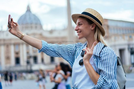 Foto de Mujer caucásica en sombrero con estilo disfrutando de vacaciones viaje rodaje vídeo vlog para compartir contenido de los medios de comunicación a las redes sociales, mujer alegre posando mientras hace clic en selfie fotos en la ciudad del Vaticano - Imagen libre de derechos